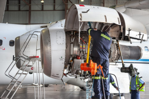 Three mechanics repairing a plane engine in the hangar