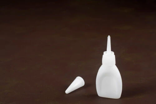 White Plastic Bottle with Cyanoacrylate Adhesive Inside on Brown Shelf Background